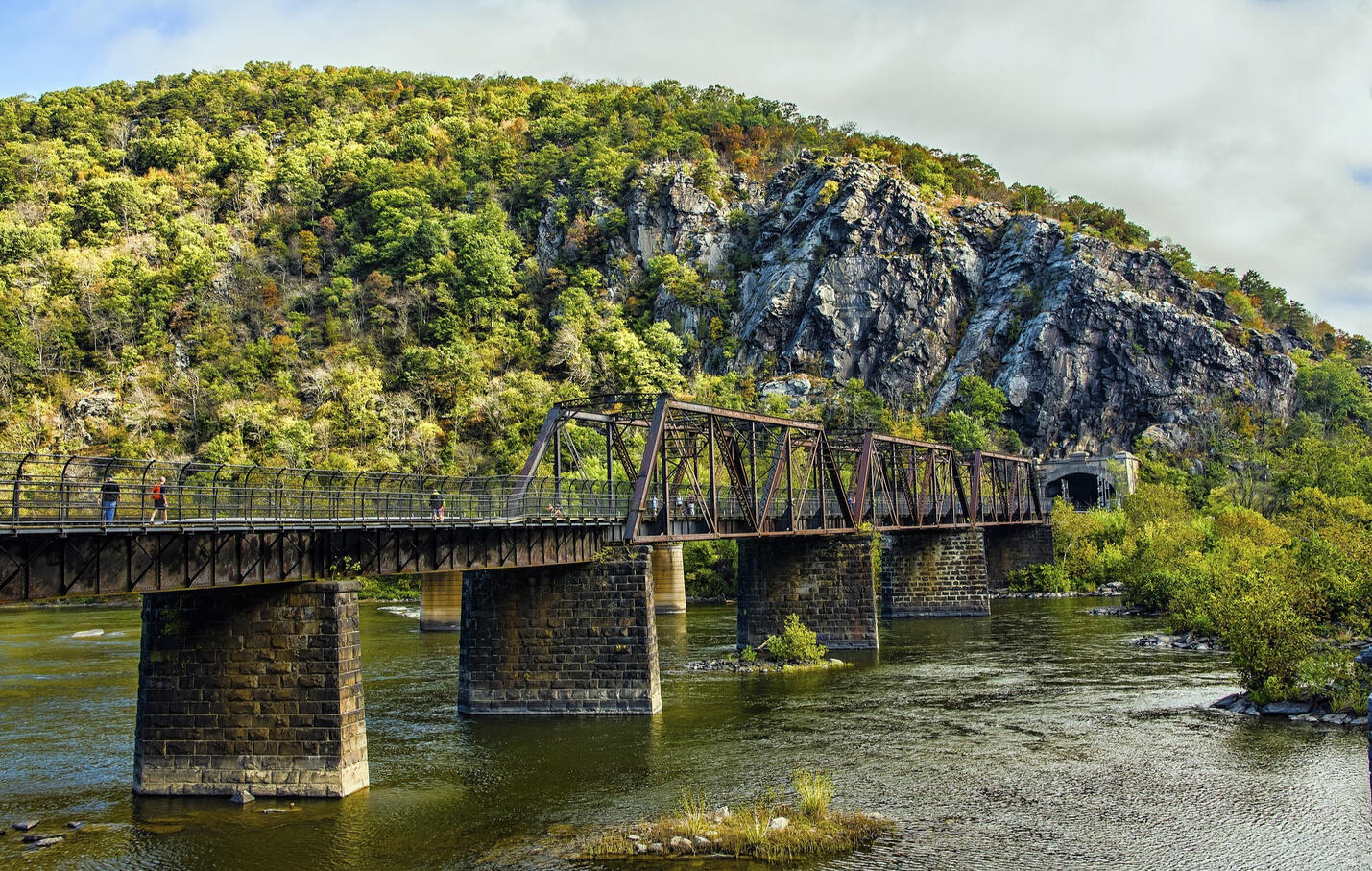 Photo of the Bridge over the Potomac River at Harper's Ferry with the tunnel into a green rocky mountain behind the bridge.