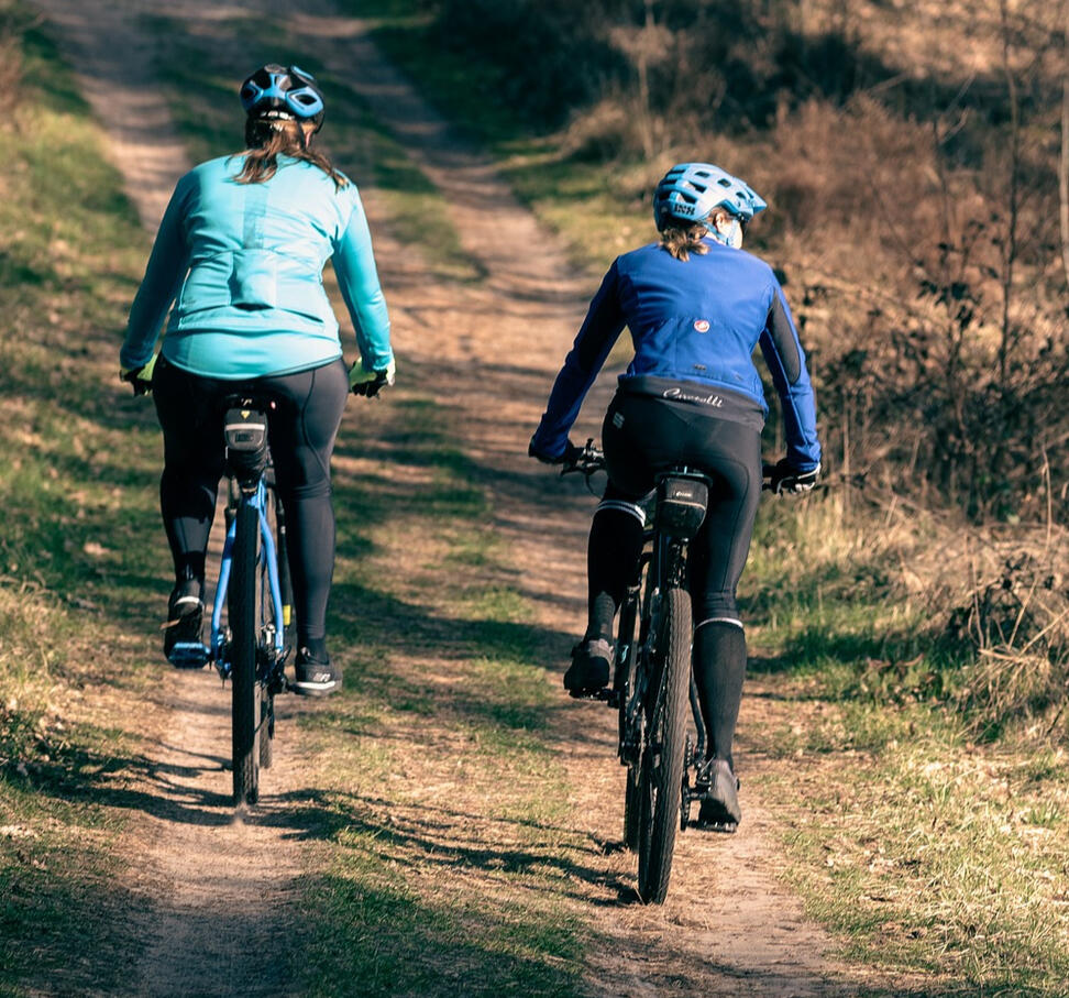 Two people biking in blue outfits and helmets along a gravel path with grass along the sides